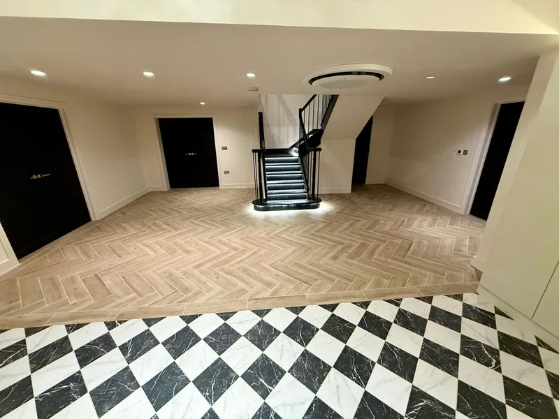 Hall with black and white marble-effect chequer tiles meeting a herringbone floor, with a black staircase with lit treads beyond